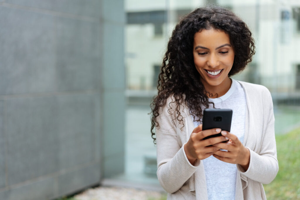 Young woman walking and using a mobile phone smiling with pleasure as she reads her total rewards statement