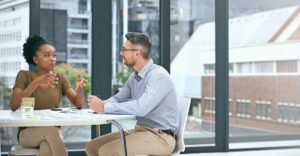Two professionals having a thoughtful discussion in a modern office setting, conveying collaboration and strategy around total rewards planning