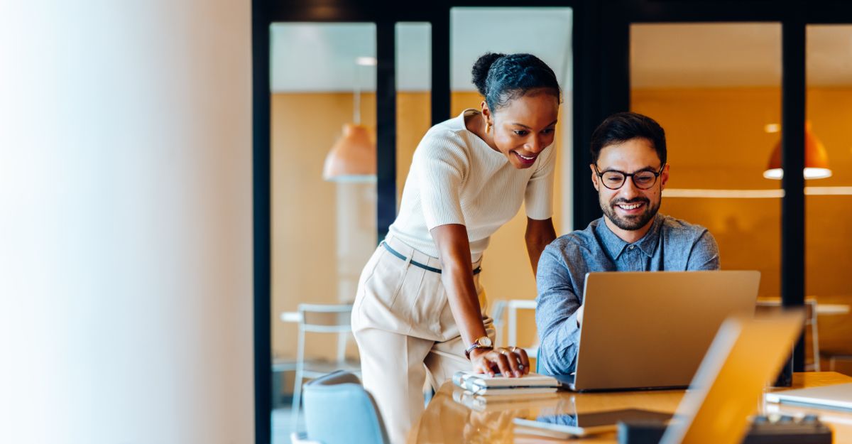 Two professionals reviewing compensation management software on a laptop in a modern office