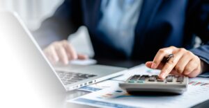 Business professional using a calculator and laptop to analyze financial charts, symbolizing how HR leaders calculate the ROI of compensation software for global enterprises.