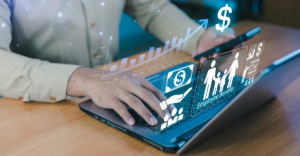 Person in business attire working on a laptop displaying holographic icons for financial growth, employee benefits, and payroll management, with an upward trending chart and dollar sign symbol floating above the screen.