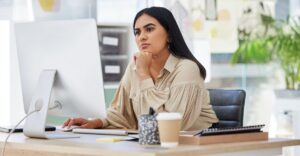An employee looking confused while reviewing her compensation statement on a desktop computer.